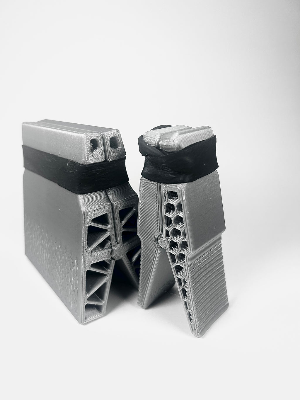 Two gray 3D-printed mechanical components or brackets with black bands, shown on a light gray background.
